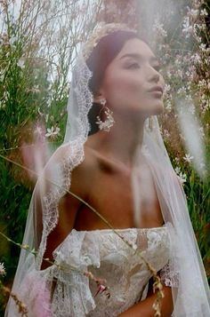 a woman wearing a wedding dress and veil standing in the grass with flowers behind her