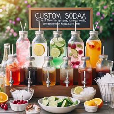 a wooden table topped with lots of bottles filled with liquid and lemons next to bowls full of fruit