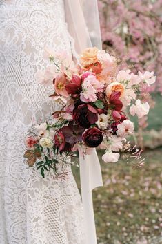 a bridal holding a bouquet of flowers in front of some pink and white blossoms