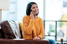 a woman talking on her cell phone while sitting on a couch in the living room