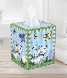 a tissue box with sheep and butterflies on it next to a stack of white towels