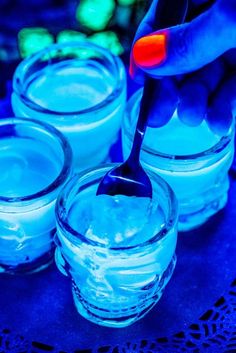 a person spooning liquid into small glass jars with blue lights in the back ground