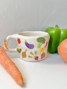 carrots, celery, and an apple sit on a counter next to a ceramic cup