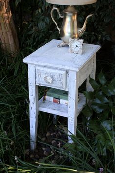 an old table with a teapot on top and books under it in the grass