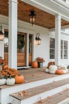 pumpkins and gourds sit on the front porch of a white house with wooden steps