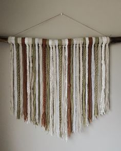 the wall hanging is made out of different colored yarns and wood sticks, which are hung on a white wall