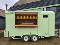 a green food truck parked in front of a building with an oven on it's side