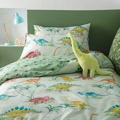 a dinosaur stuffed animal sitting on top of a bed next to pillows and pillow cases