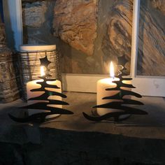 two lit candles sitting next to each other on top of a stone slab in front of a window