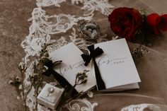 two roses and some cards on a lace table cloth next to an open ring box