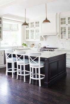 a kitchen with white cabinets and black island in front of the stove top, surrounded by stools