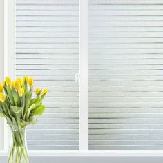 yellow tulips in a vase on a window sill with blinds behind them