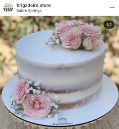 there is a white cake with pink flowers on the top and bottom, sitting on a wooden table