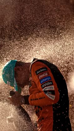 a man in an orange and black racing suit spraying water on him with his hands