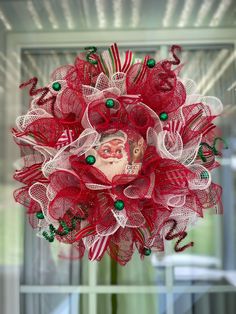 a red and white mesh wreath with a santa clause face on the front door window