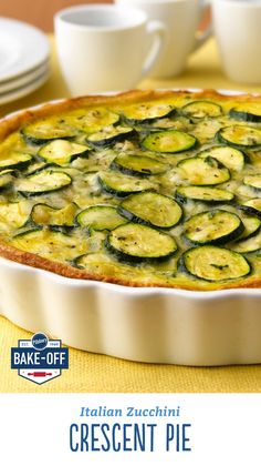 a pie with zucchini in it on a table next to cups and saucers