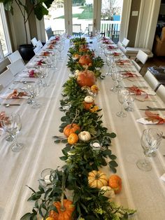 a long table is set with pumpkins and greenery