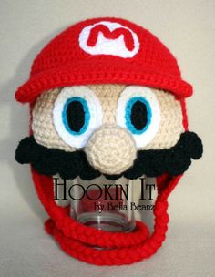 a crocheted mario hat with googly eyes and a mustache is shown in front of a white background