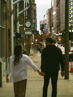 a man and woman walking down the sidewalk holding hands