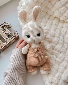 a crocheted bunny is sitting on a blanket next to a handmade letter