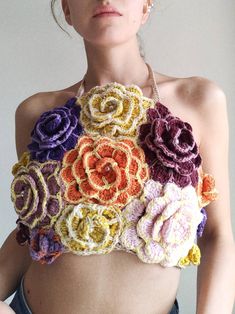 a woman wearing a crochet top with flowers on it's chest and her hands in her pockets