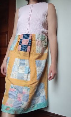 a woman standing next to a wall wearing a dress made out of patchwork material