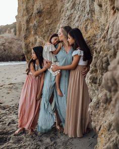 three women in long dresses hugging each other on the beach