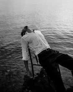 a man laying on top of a chair next to the water