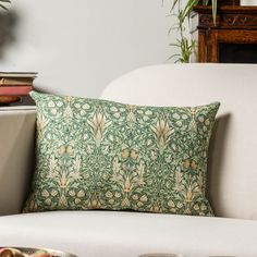 a green and gold pillow sitting on top of a white couch next to a potted plant