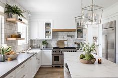 a large kitchen with white cabinets and marble counter tops, an island in the middle is surrounded by potted plants