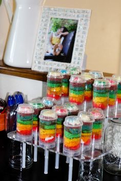 there are many different colored desserts in plastic containers on the table with pictures behind them