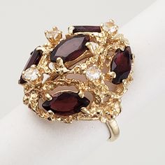 "A 14K gold attention grabber! This vintage domed cocktail ring has a regal combination of lacy, shimmering gold, rich red color, and sparkle. It features five marquise cut garnets and four rock crystal accent stones. Vintage: 1980s - 1990s Size: 4 on the loose side Materials: 14K Gold, Garnets, Rock Crystal Marked: 14K (marked and tested) 5 Garnets: marquise cut, 8mm x 4mm ea. 4 Rock Crystal: round, approx. 2.5mm ea. Width North to South: 7/8\" Width East to West: 3/4\" Stands Off Finger: just Attention Grabber, Vintage Cocktail Ring, Garnet Jewelry, Pin Pendant, Vintage Cocktail, Multi Stone Ring, Marquise Cut, Rock Crystal, Diamond Sizes