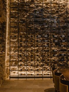 a dining room table and some chairs in front of a wall made out of wine bottles