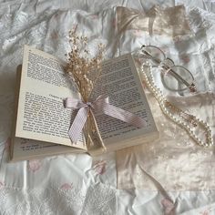 an open book on a bed next to a pair of eyeglasses and some flowers