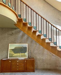 a wooden dresser sitting under a stair case next to a bannister with a painting on it