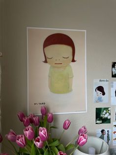 a vase filled with pink tulips next to a wall covered in pictures and photos