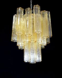 a chandelier made out of yellow glass pieces hanging from a chain on a black background