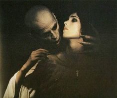 a man and woman in the dark with one holding his head to her chest while the other is looking at him