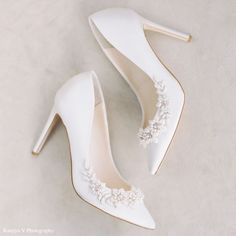 white wedding shoes with flowers on the side and heels that are pointed out to the side