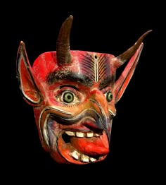 a red mask with horns on it's head and two green eyes in front of a black background