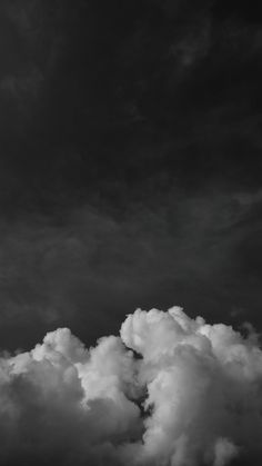 black and white photograph of an airplane flying in the sky with fluffy clouds around it