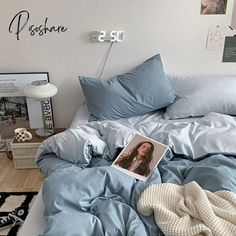 an unmade bed with blue sheets and blankets on it, next to a clock