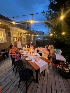 a group of people sitting around a wooden table on a deck eating food and drinking wine