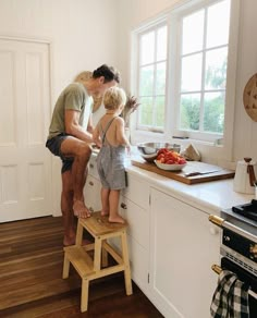 a man and two children are standing on a stool in the kitchen