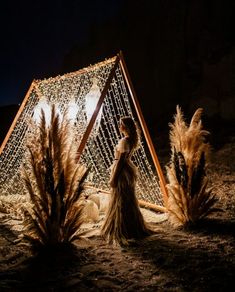 a woman is standing in the sand near some tall grass and an object with lights on it