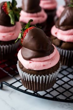 chocolate cupcakes topped with pink frosting and strawberries on a wire rack