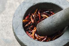 a mortar bowl filled with red peppers on top of a cement floor next to a black object