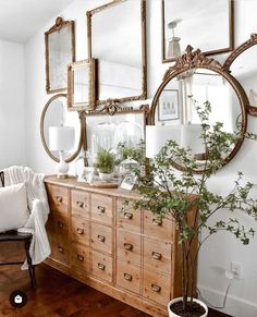 a wooden dresser sitting next to a mirror on top of a wall with lots of mirrors above it