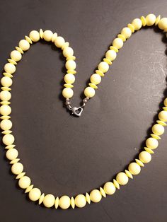 "Vintage. Summery. Sunny Yellow Beaded Necklace with round beads separated by disk beads of the same color and material. Very lightweight, maybe Lucite. Strung on cotton thread. 24\" long single strand with a unique heart spring ring clasp in silvertone. Round beads are 3/8\". Very good condition. Such a unique beaded necklace!"