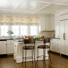 a kitchen with white cabinets and black counter tops, two stools in front of the island